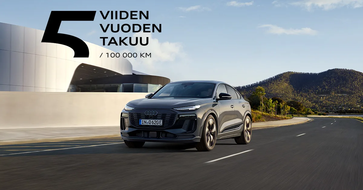 Audi quattro ajaa keväisellä maantiellä modernin rakennuksen edestä.