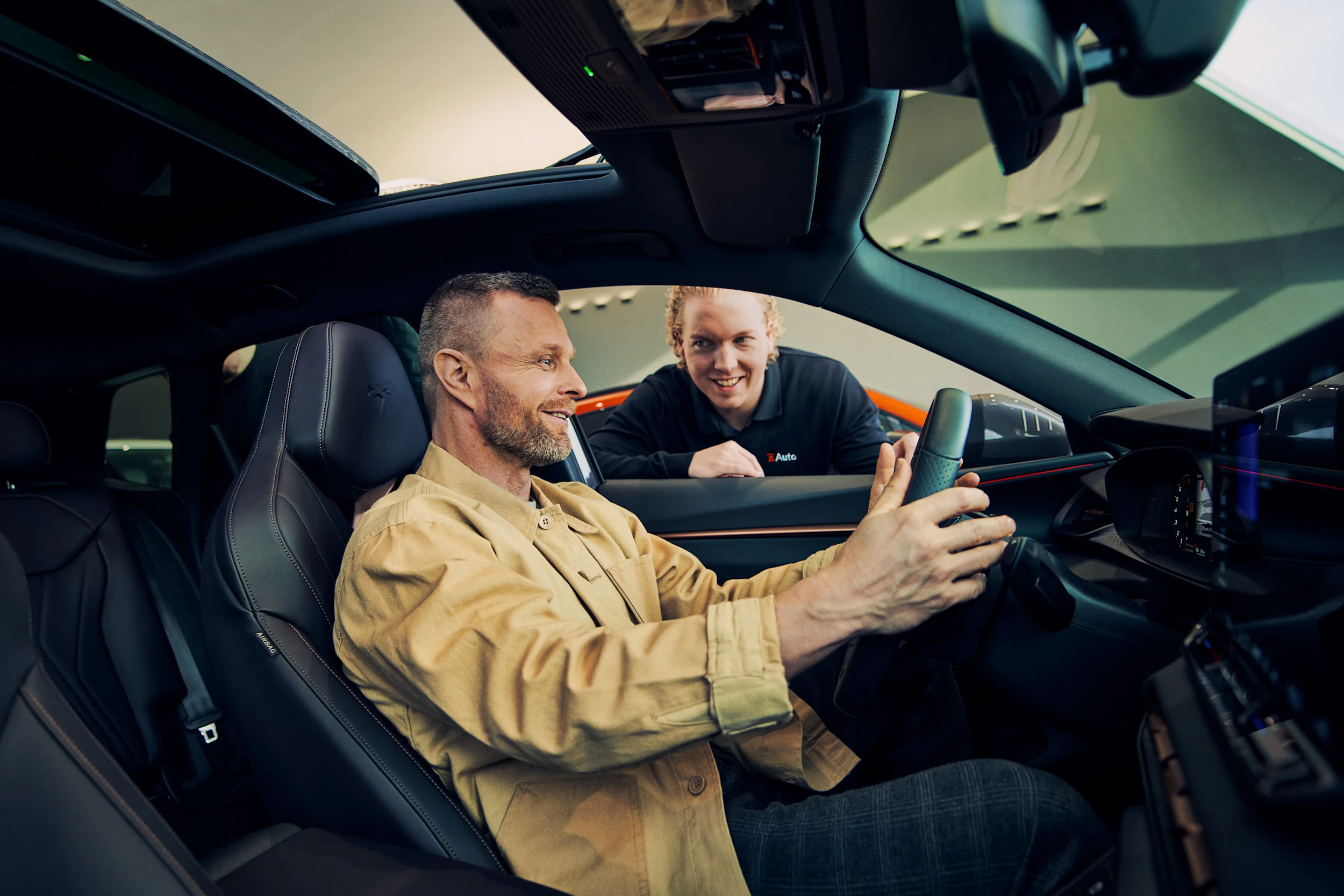 Mies istuu autossa kuljettajan paikalla kun K-Auton myyjä esittelee hänelle autoa.