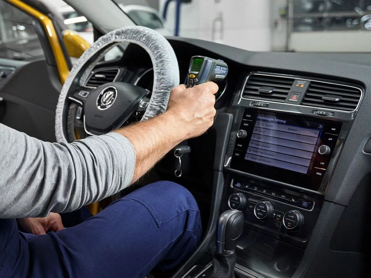 Ammattilainen suorittamassa auton ilmastointihuoltoa testaustyökalulla