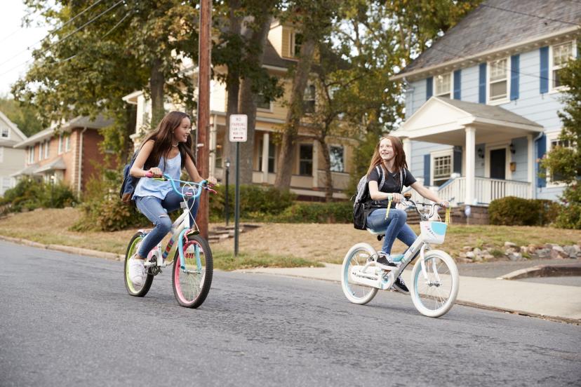 Two girls riding their bicycles in the neighborhood.
