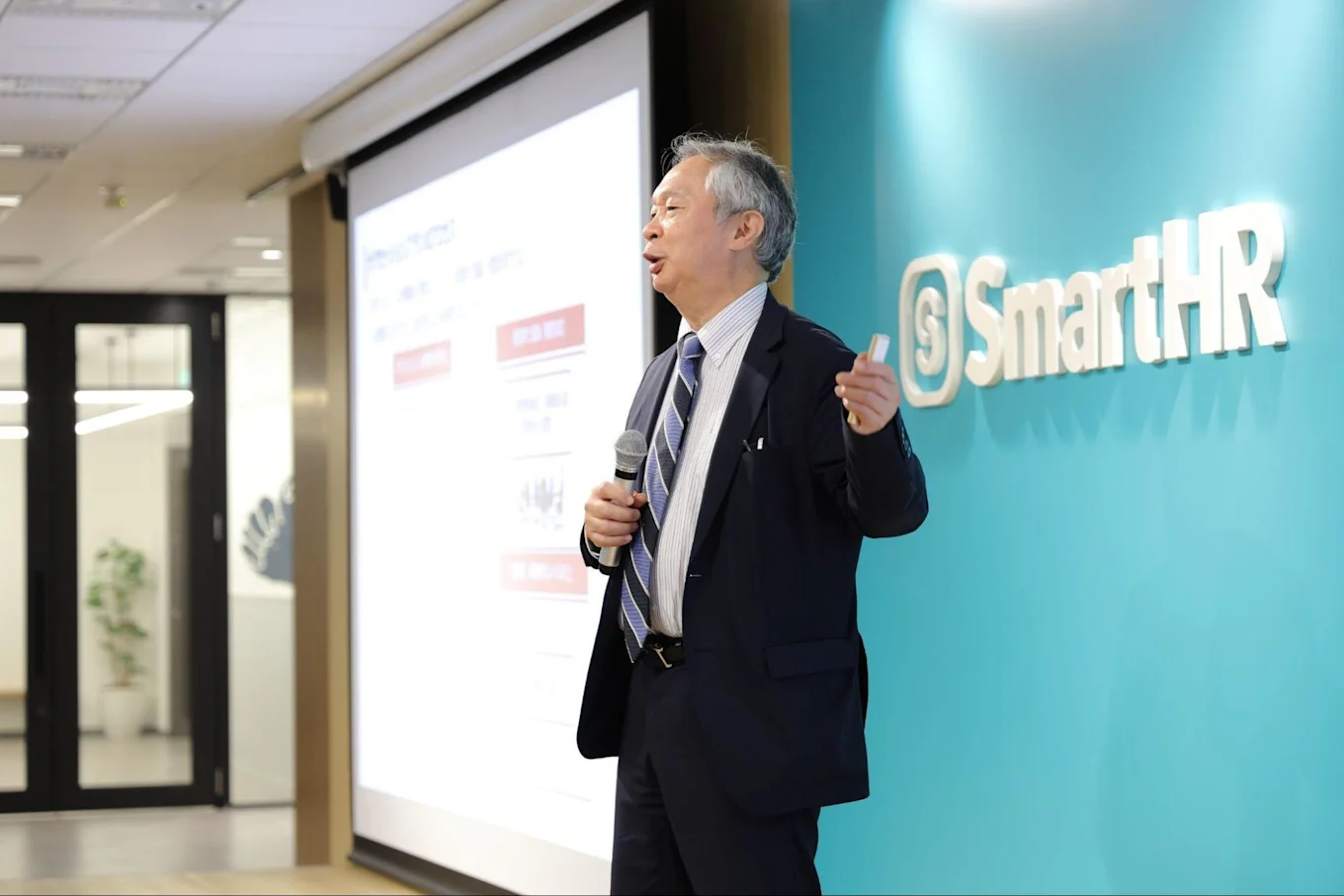 マイクを手に大きく左手を広げながら聴衆に向けて話す有沢さん