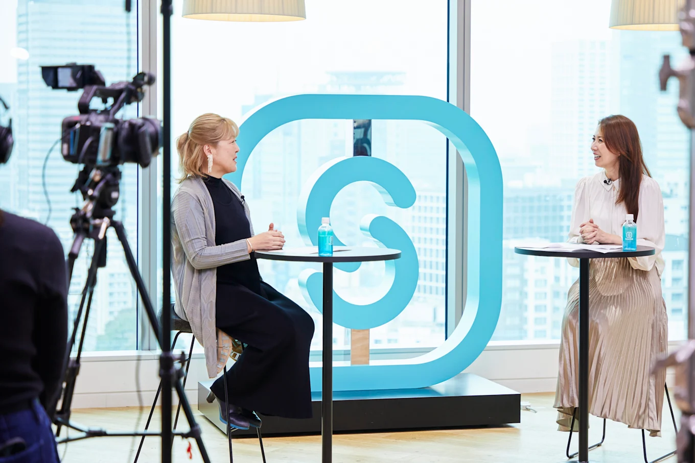 SmartHRオフィスのロゴ前で対談している堀井さんと笹原さんを撮影している様子。手前にはカメラなどの撮影機材が写っている