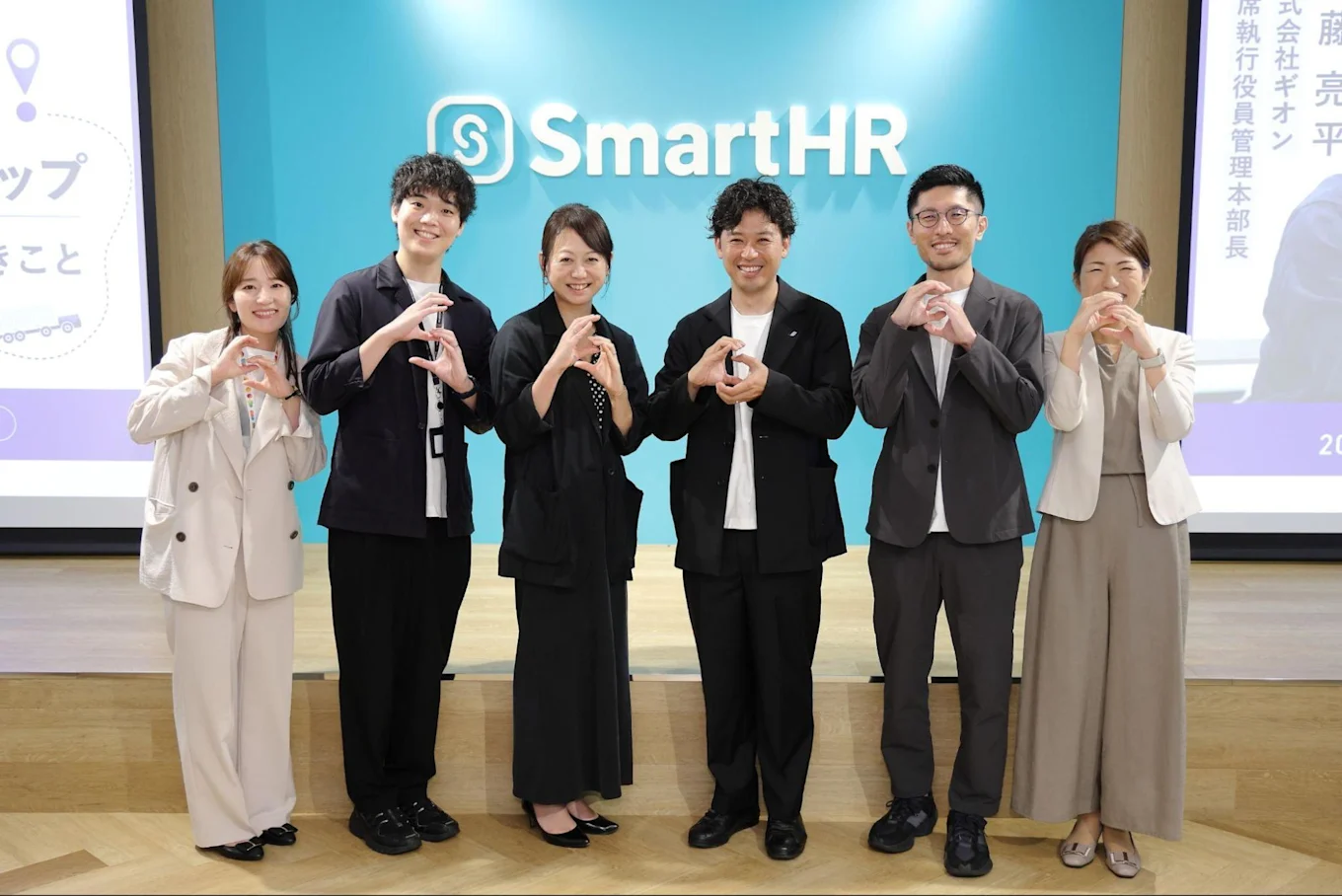 SmartHRのロゴ前で、手でハートポーズを作って並ぶ6人の男女