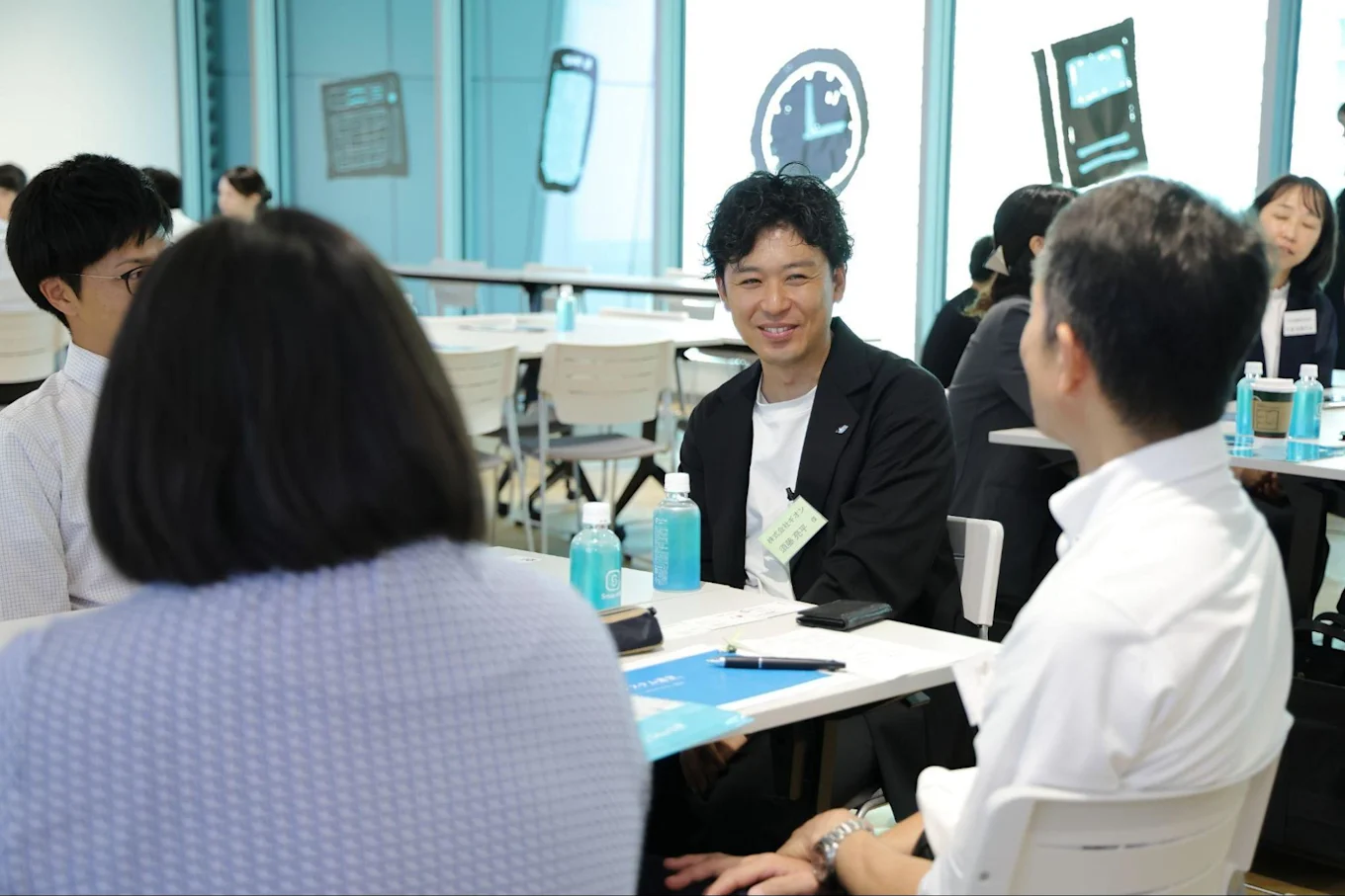SmartHRロゴ入りのペットボトルが置かれたテーブルで、笑顔で参加者と会話する須藤さん