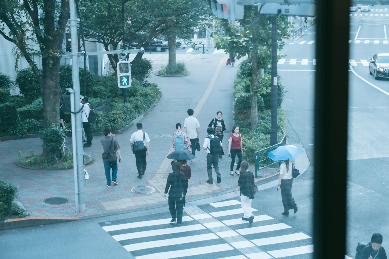 建物の窓から、横断歩道を渡る人々を見下ろしている写真。