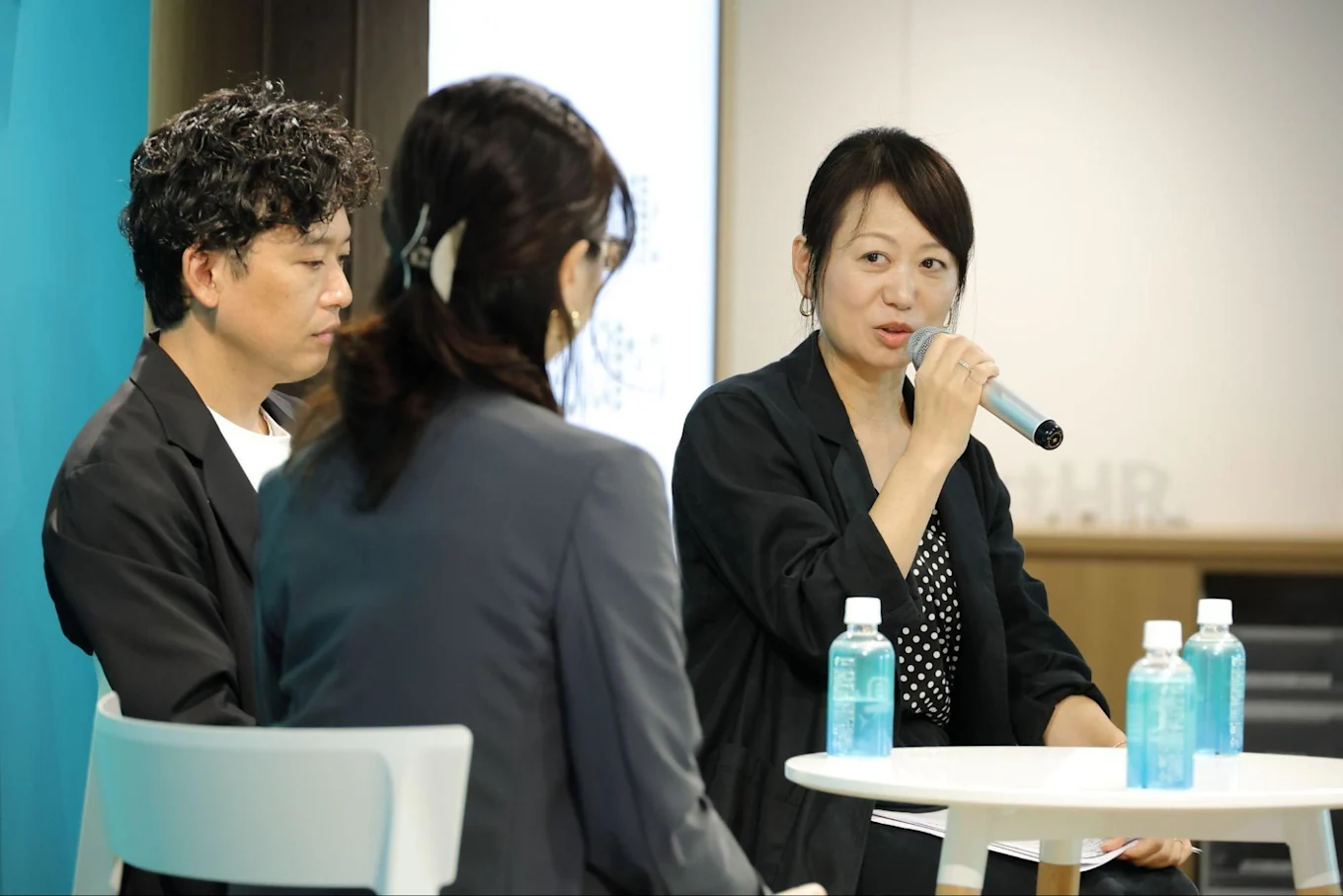 テーブルの前でマイクを持って話す渋谷さんと、その隣に座る須藤さん、松栄