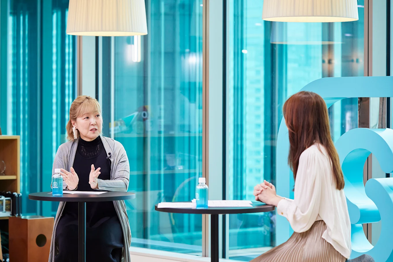 対談中の笹原さんと堀井さん、両手を10cmほど小さく広げるジェスチャーをする笹原さんと堀井さんの後ろ姿