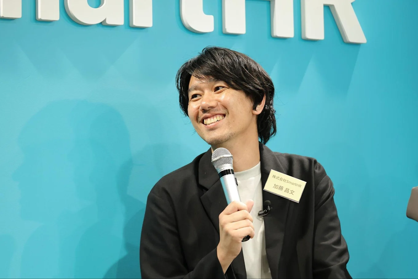 マイクを持ちながら笑顔で話す加藤さんの写真