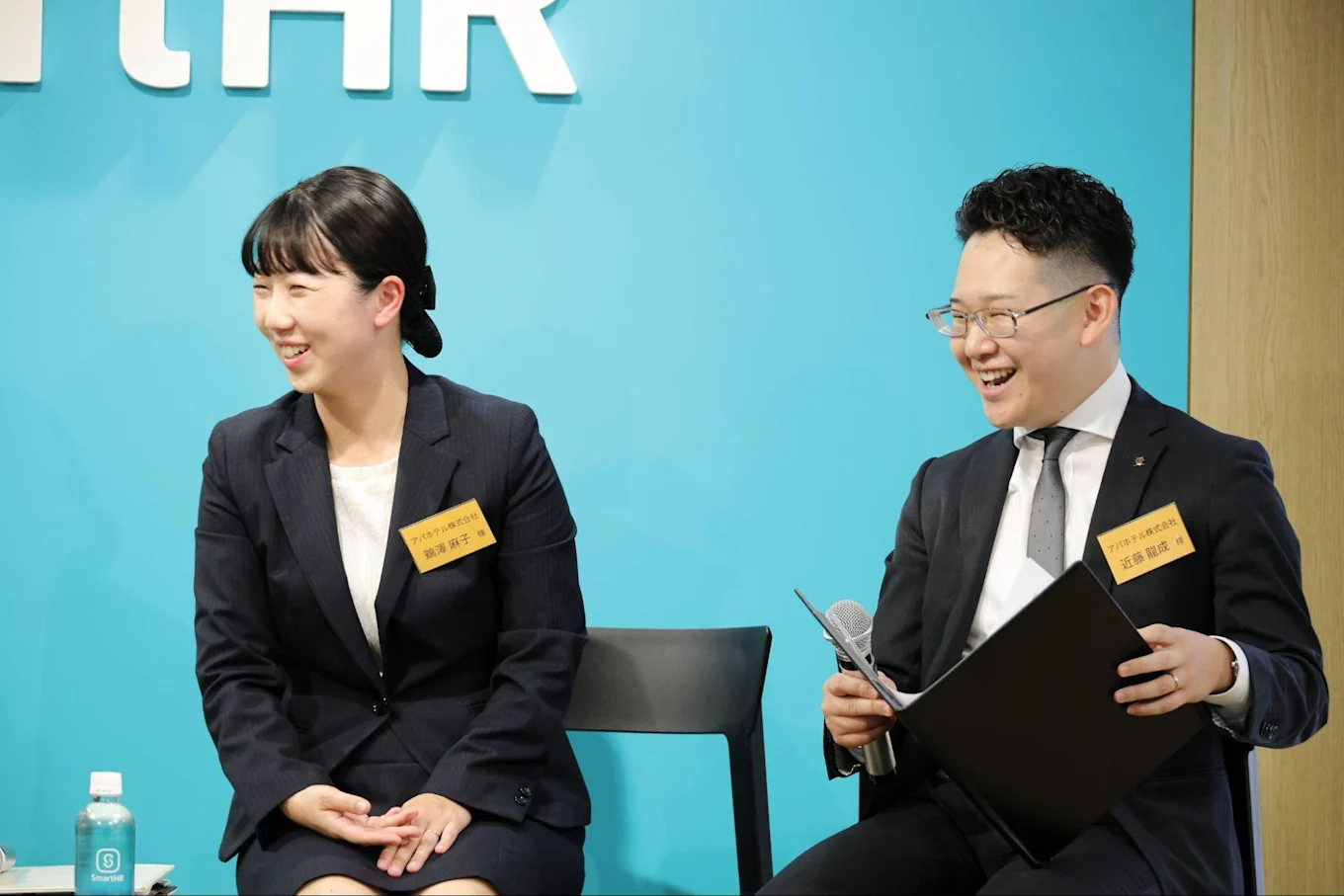 左から鵜澤さん、マイクとバインダーを持った近藤さん。2人とも笑顔で右を向いている。