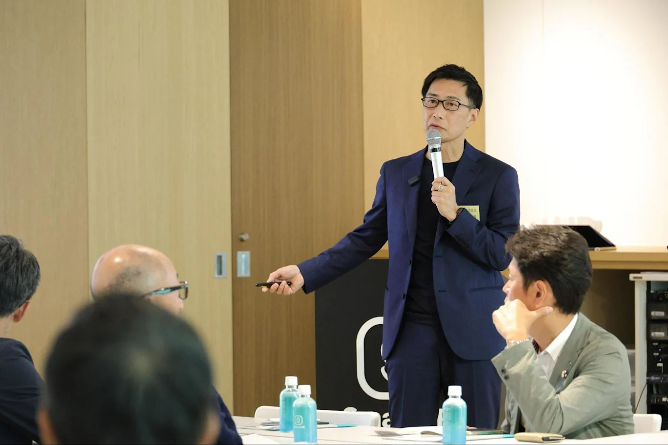 セミナーや研修の会場で、マイクを持ちながら前方に立って話す西田さんの様子。