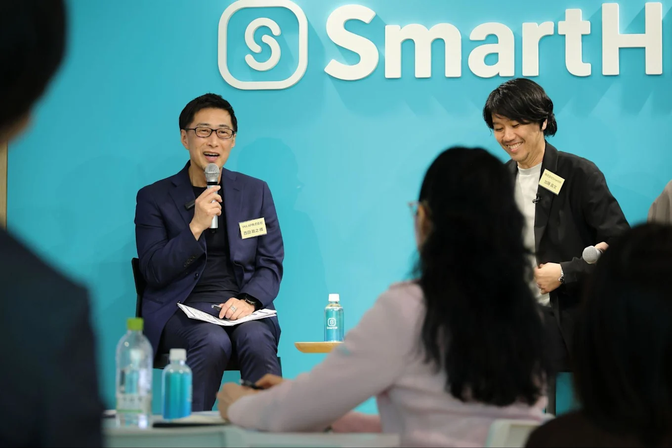 椅子に座りながらマイクを持って話す西田さんとその隣で椅子に座りながら笑顔で聞いている加藤さんの写真