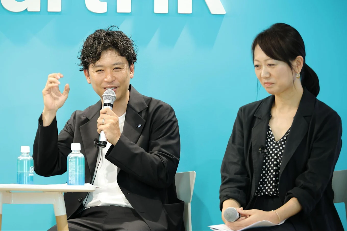 マイクを持ちジェスチャーを交えて話す須藤さんと隣に座る渋谷さん