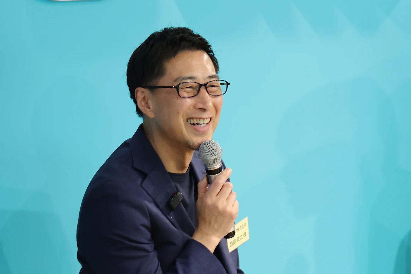 満面の笑顔でマイクを持ちながら話す西田さんの写真