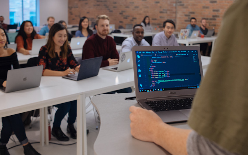 Instructor with laptop teaching Web Development Bootcamp students in classroom