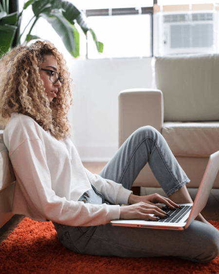 Student sitting on the floor of a living room using their laptop.