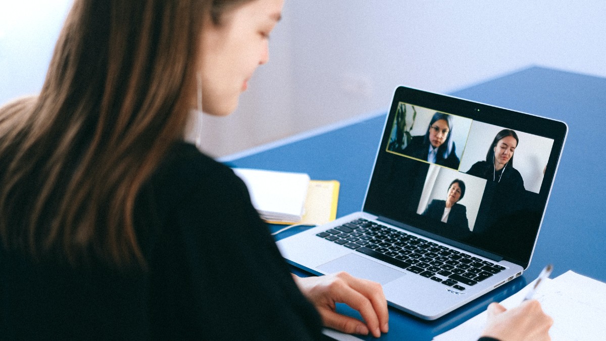 Person in a video interview with two professionally dressed people. They're taking notes at their desk.