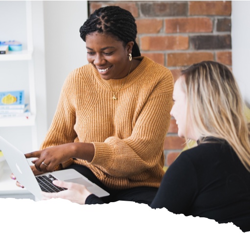 Director of Outcomes, Chi-Chi Egbo, is working with a Juno student. Chi-Chi is smiling, pointing at the screen of a Macbook Pro, and the student is nodding along with her explanation.