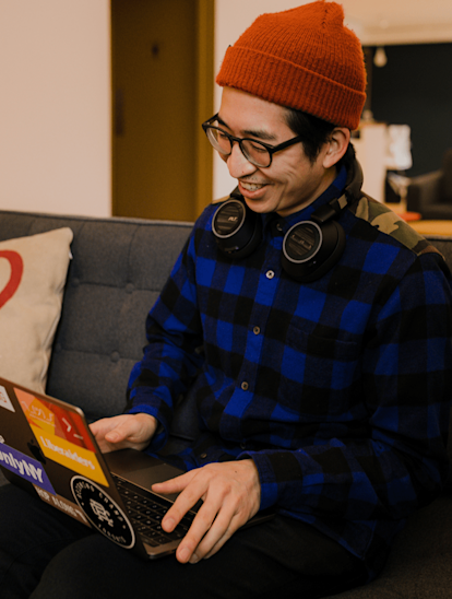 Juno's Community Manager Brandon Keen sits on a grey couch at Coral working on his laptop.