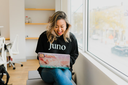 A woman smiling excitedly at her laptop, wearing a Juno-branded sweatshirt