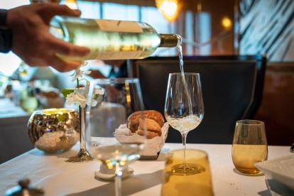 A hand pouring wine into a glass at a restaurant