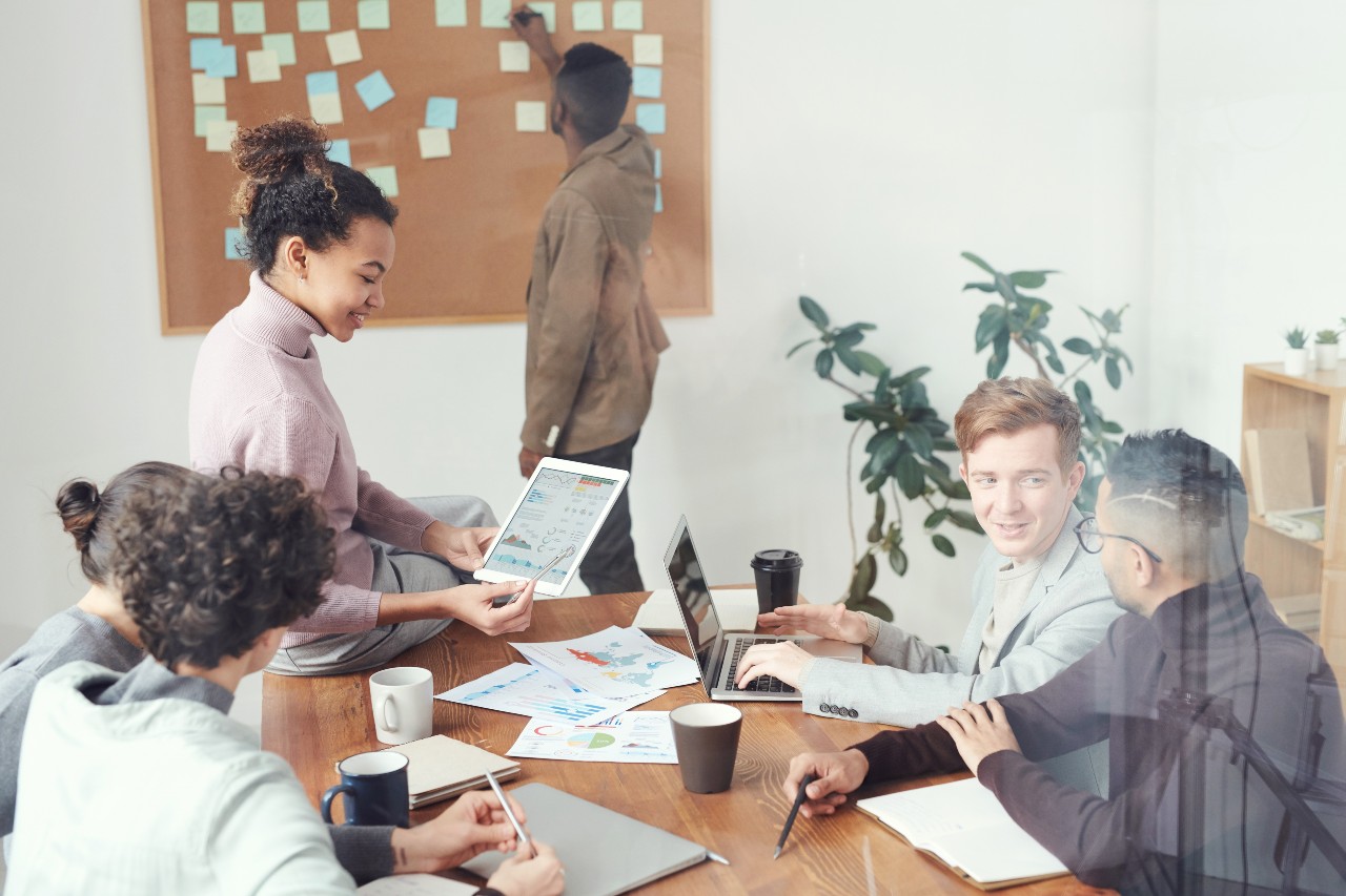A group of young colleagues working together in a conference room. There are sheets of paper with graphs and data charts on them.