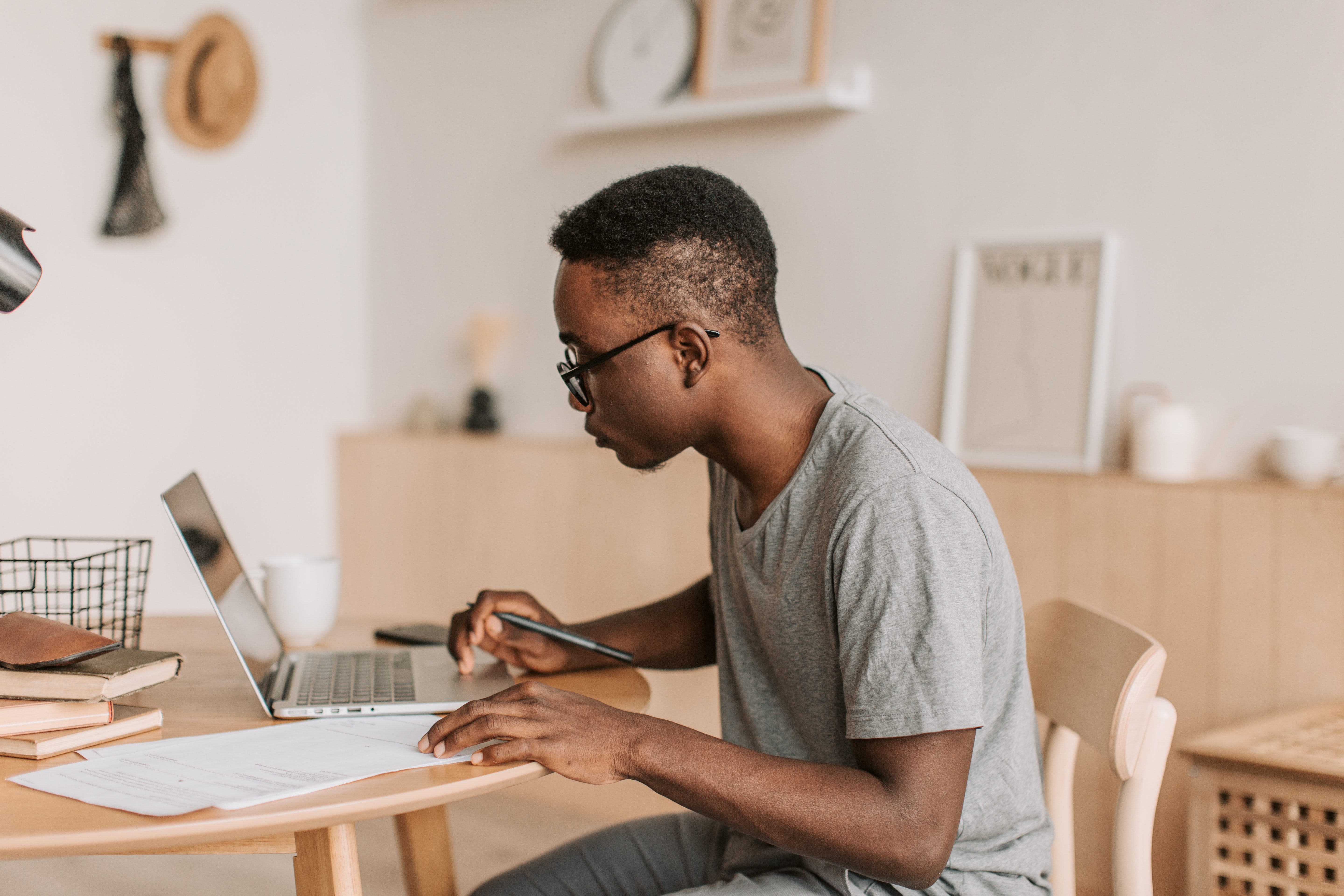 young man at his desk looking at his laptop computer, pen in hand and some papers in front of hime