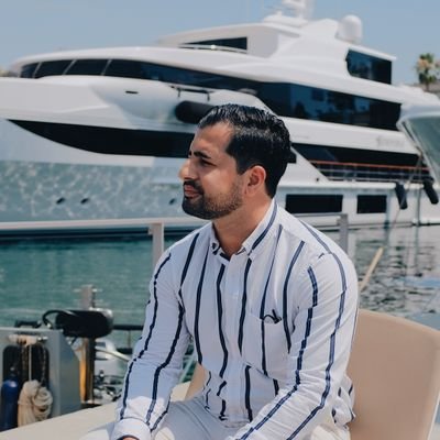 Shahyn Kamali sitting outside by a marina, with a cruise ship in the background