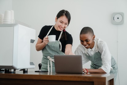 Two baristas smiling at a laptop