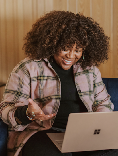 Juno College student wearing a grey and black plaid jacket is smiling at a laptop camera