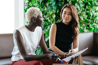 Two professional women talking together on a couch with paper and pen