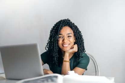 Woman with glasses sitting in front of laptop smiling at the camera
