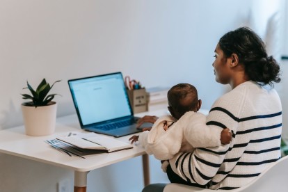 A parent sitting at their laptop on a desk with their child