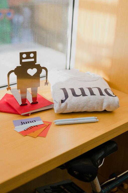 A Juno branded sweater, some pens, and business cards are laid out next to a friendly looking robot.