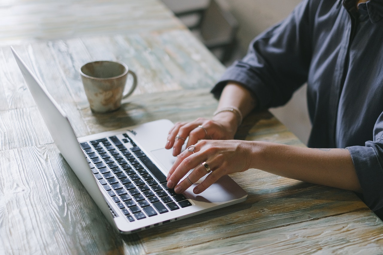 Hands typing on laptop with a tea cup beside it