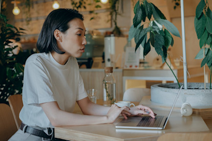 A woman typing on her laptop in a cafe, surrounded by potted plants.