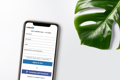A cellphone with a LinkedIn account signup page on its screen. A monstera plant leaf lies beside it.