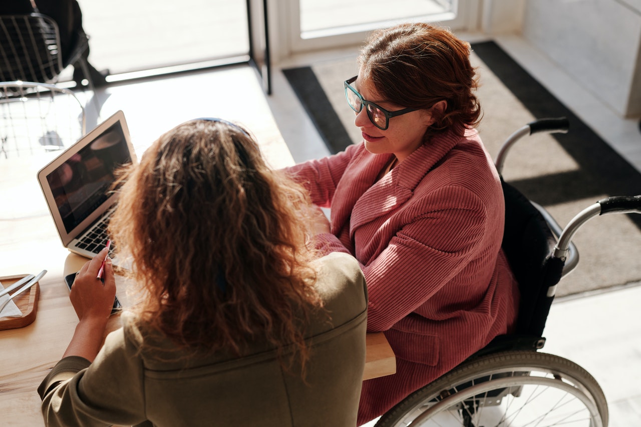 Woman in wheelchair on laptop talking to another woman