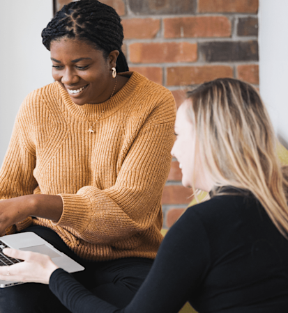 Chi-Chi Egbo, wearing a yellow sweater, is working with a student on her laptop.