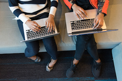 Overhead shot of two women sitting on a couch typing on their laptops