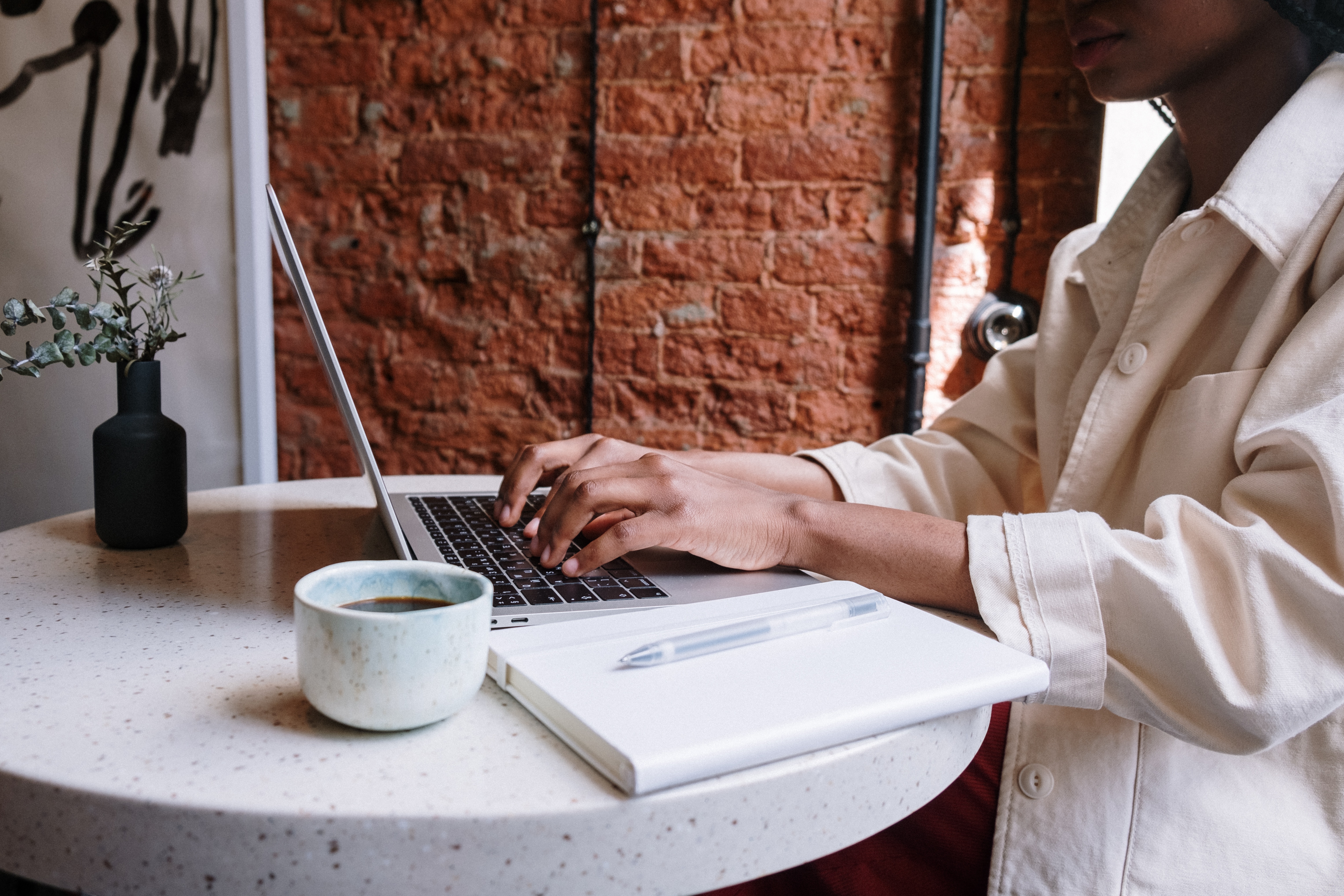 A person working on their laptop with a notebook and cup of coffee