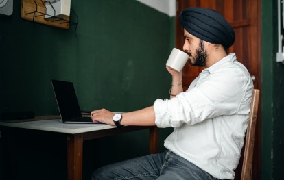 Man sipping coffee in front of laptop on desk