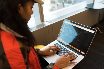 A woman in a black and red jacket coding on a laptop