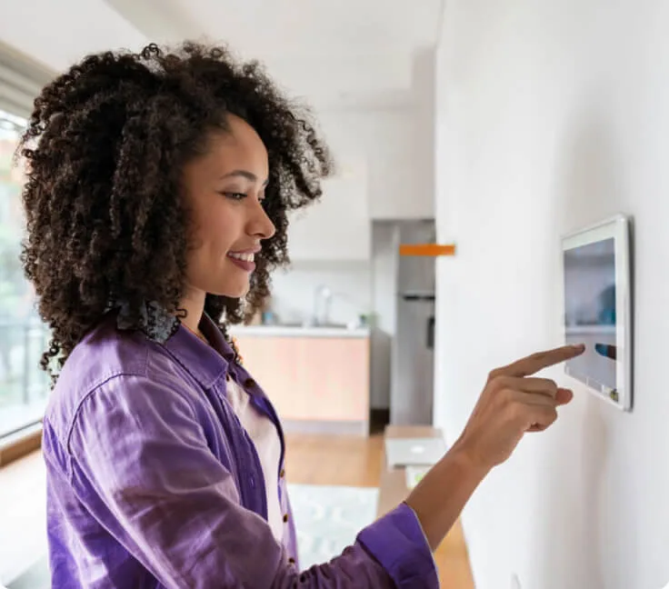 A smiling woman using a wall-mounted security touchpad to control her TELUS SmartHome Security system.