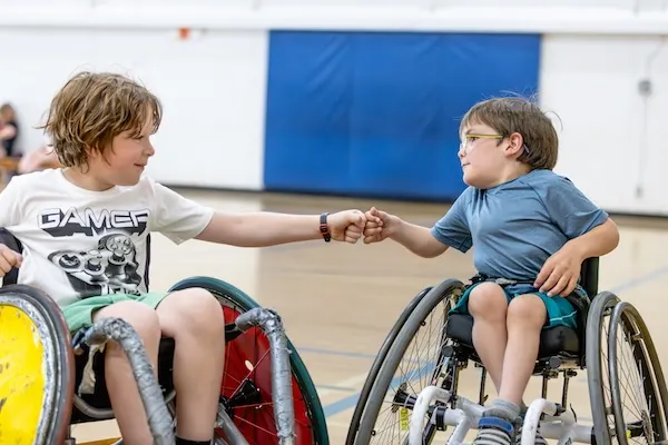 Two students giving a fist pump while playing wheel chair basketball.