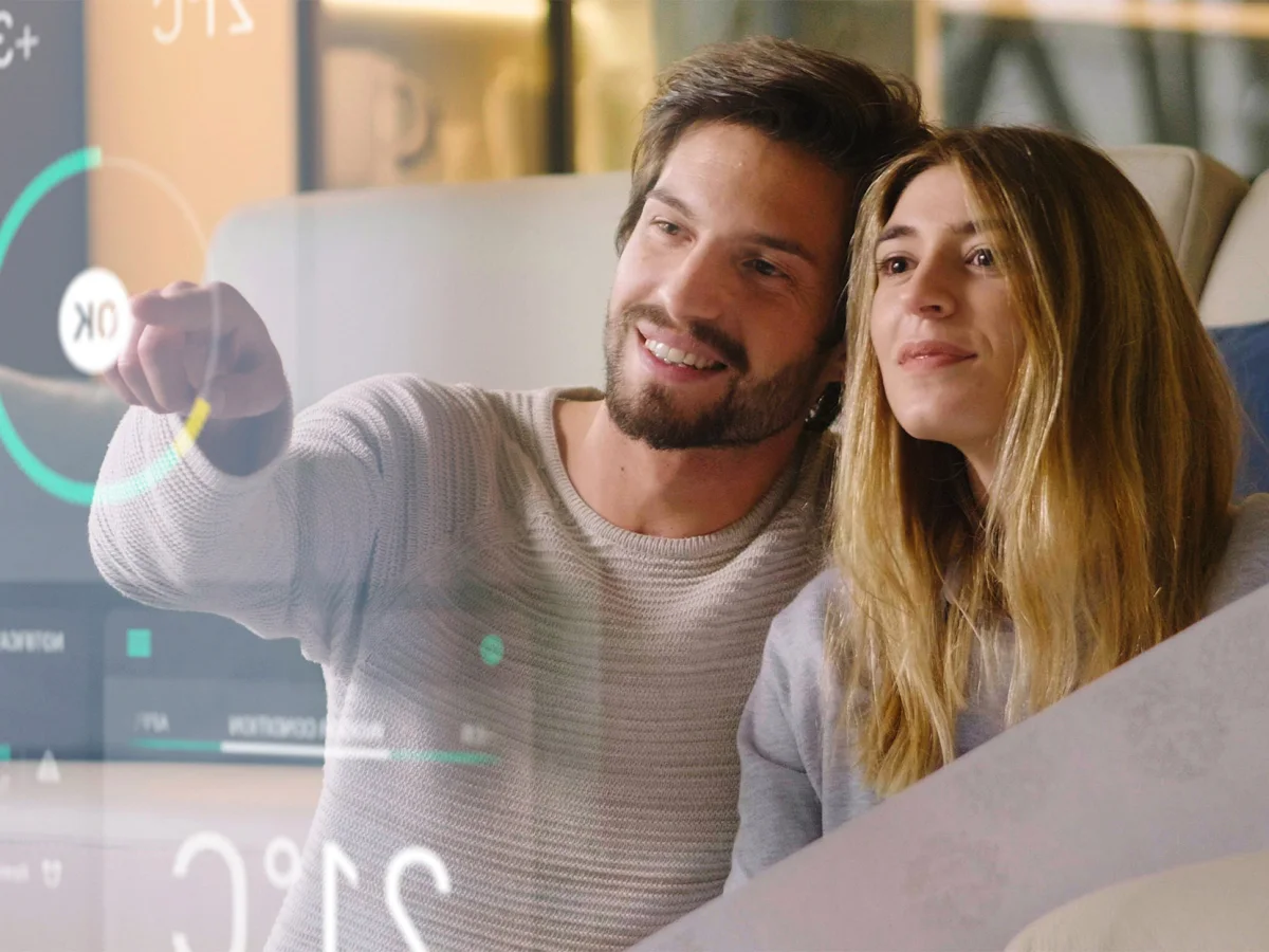 Une femme et un homme souriants pointant un grand écran transparent