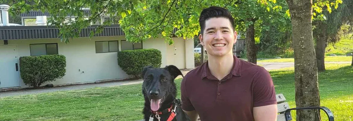 An individual sits outside next to his dog