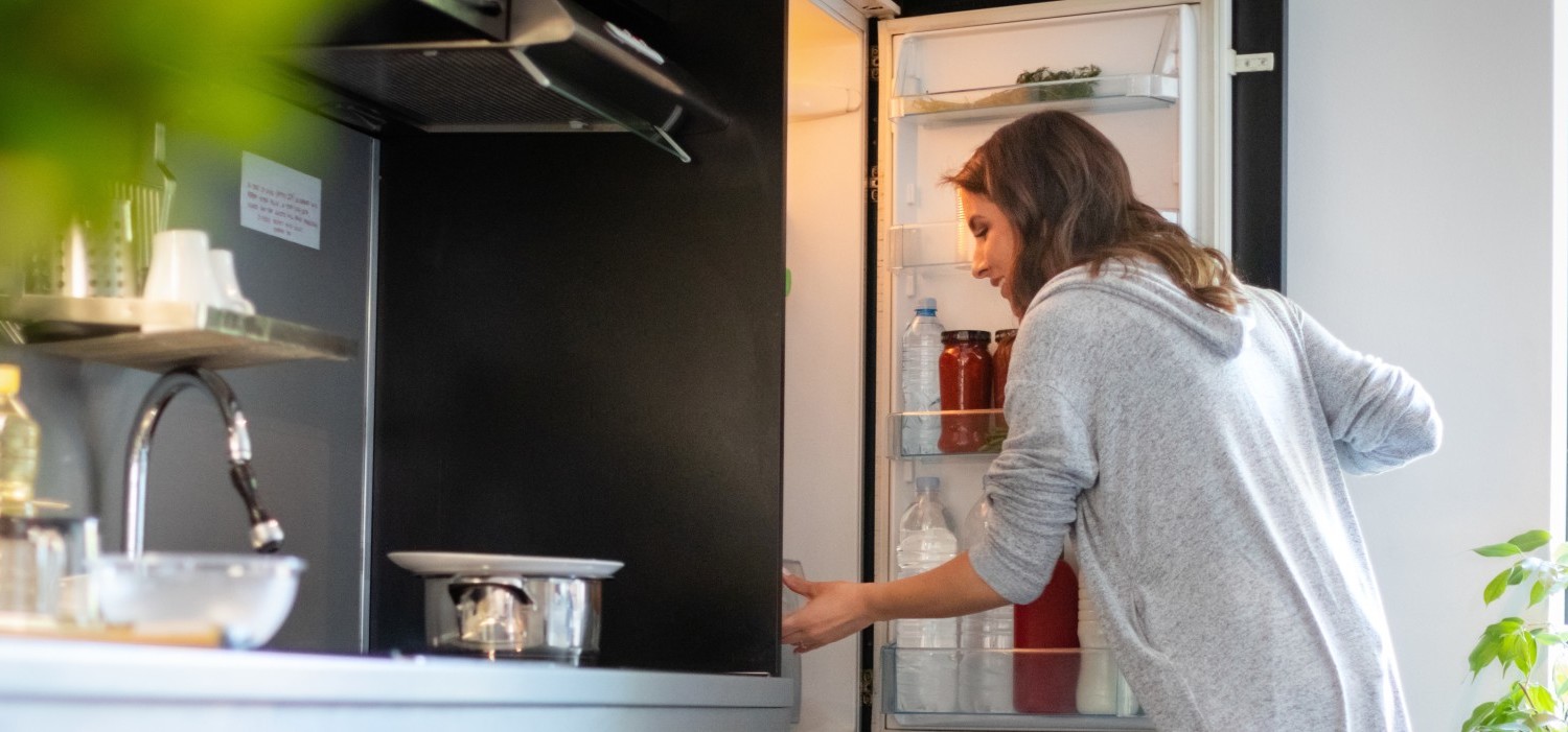 Une femme ouvre son réfrigérateur dans sa cuisine et se prépare à planifier ses repas pour réduire le gaspillage alimentaire.