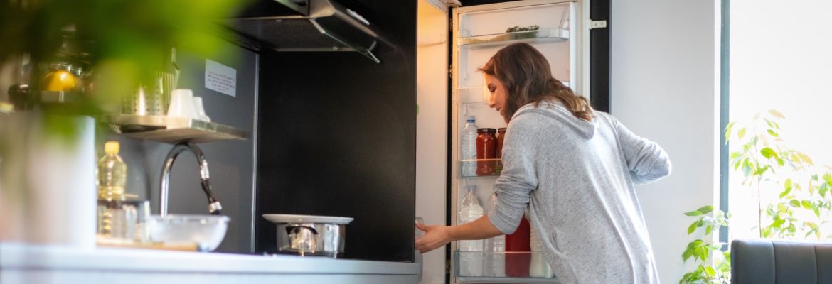 Une femme ouvre son réfrigérateur dans sa cuisine et se prépare à planifier ses repas pour réduire le gaspillage alimentaire.