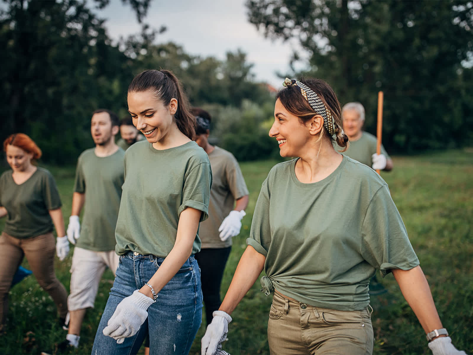 Volunteers in green shirts doing garden work walking through a field.
