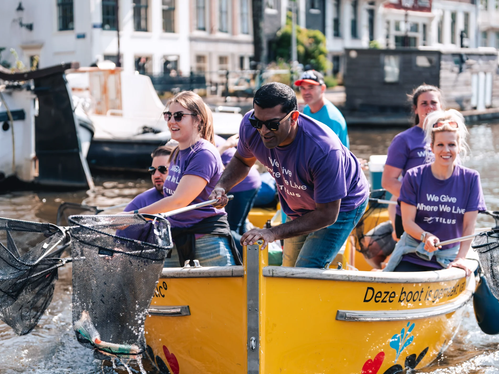 TELUS team members on a boat, using a net to collect plastic waste from a canal.

